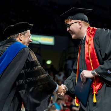 Dean Chris Martin shaking a male student's hand at graduation