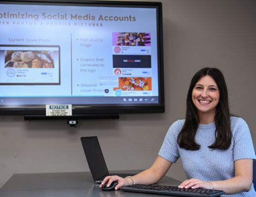 A female student sitting at a table on a computer with a screen behind her