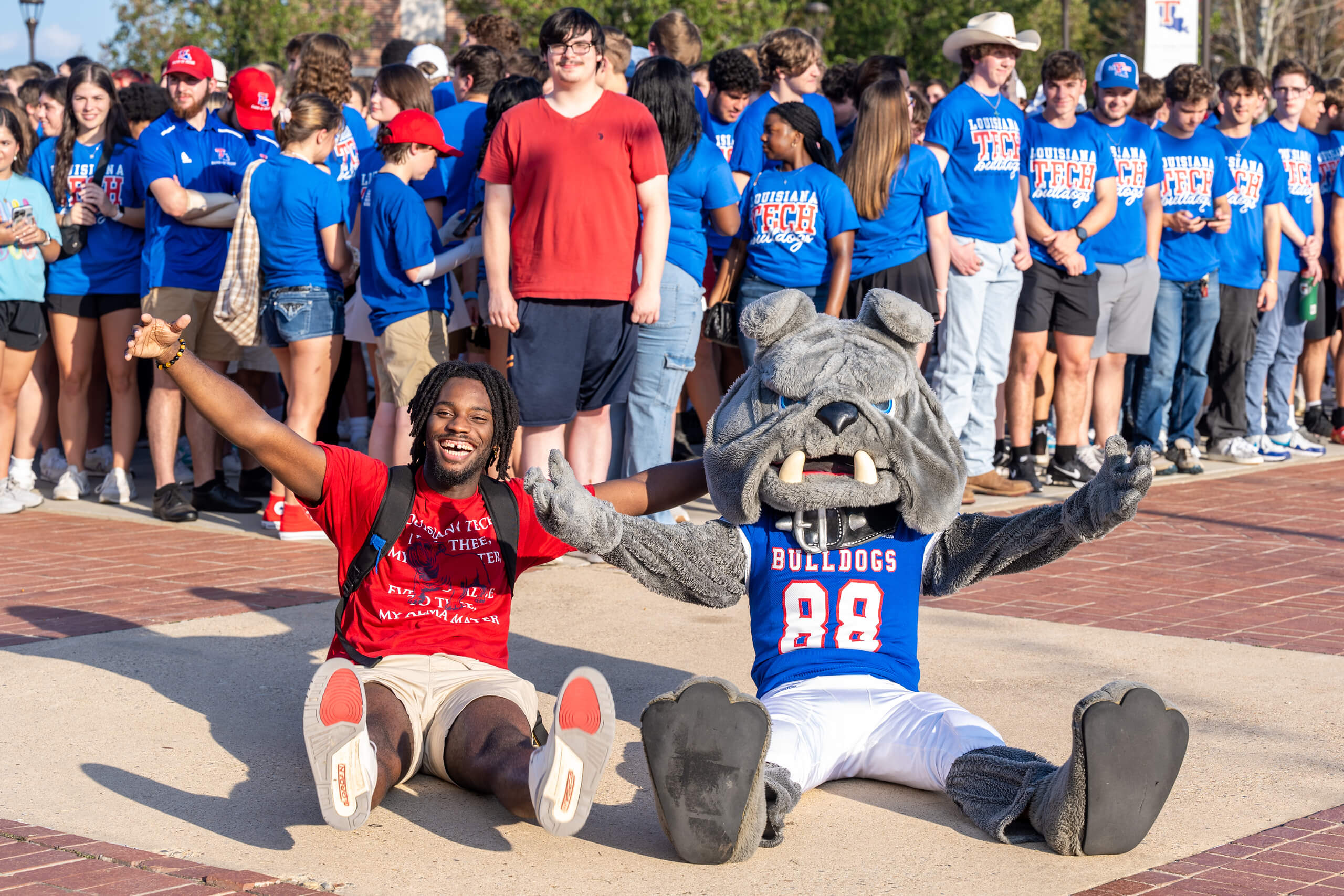 A student and the LA Tech mascot sit together and smile