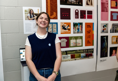 female graphic design student standing in front of poster of work