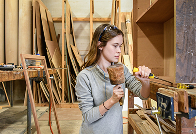 A student creates wood furniture in the workshop.