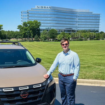 Dylan Watson standing next to a Nissan vehicle in front of the Nissan headquarters
