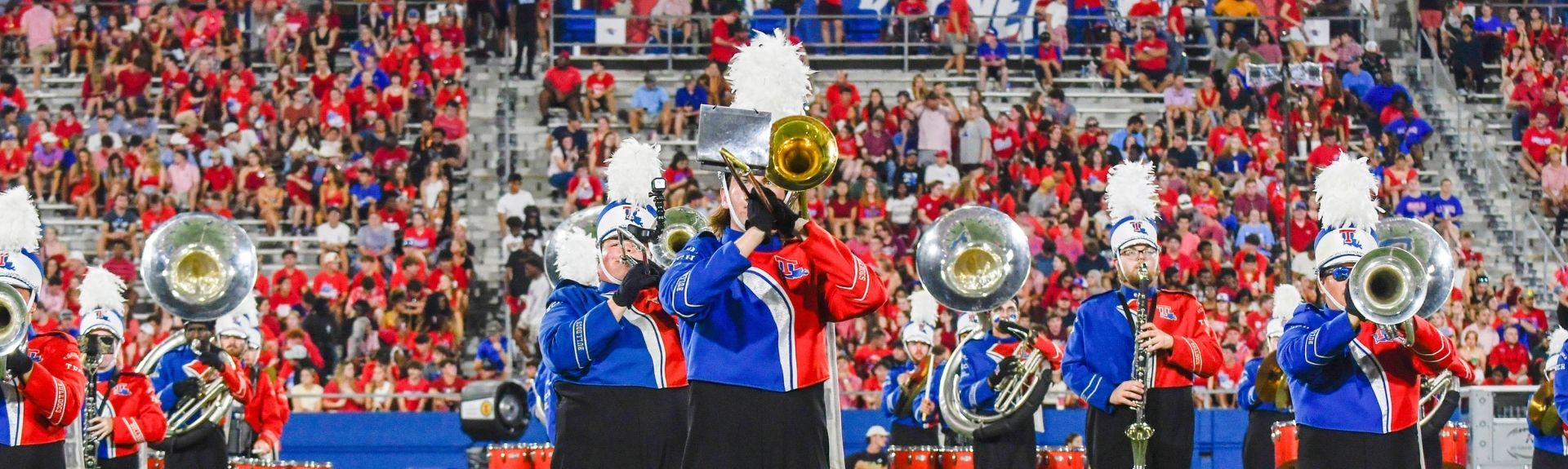 band of pride playing on the football field with fans in the back 