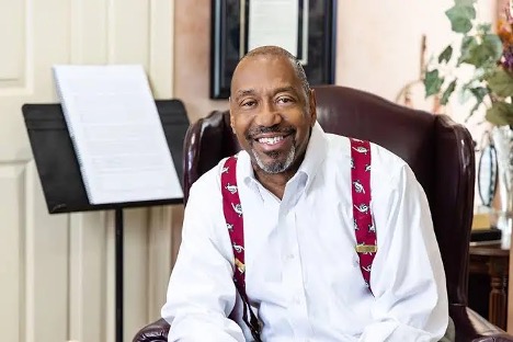 image of Quincy C. Hillard sitting in a brown leather chair with a music stand behind him 