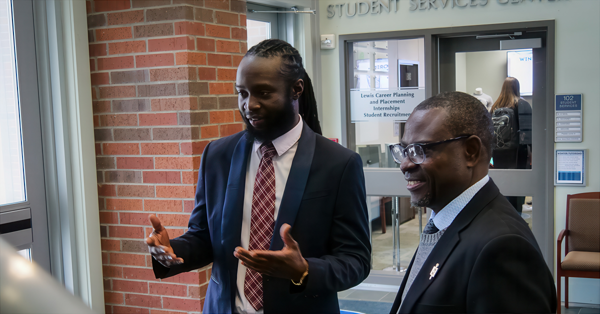 A man stands with another man engaged in conversation inside of the Louisiana Tech College of Business lobby.