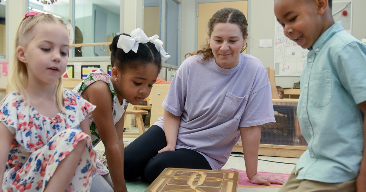 A college student plays with small children on the floor of a classroom
