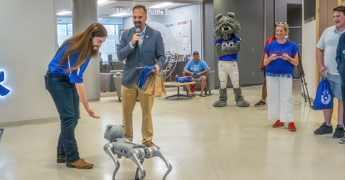 A student leans to shake hands with a robot bulldog