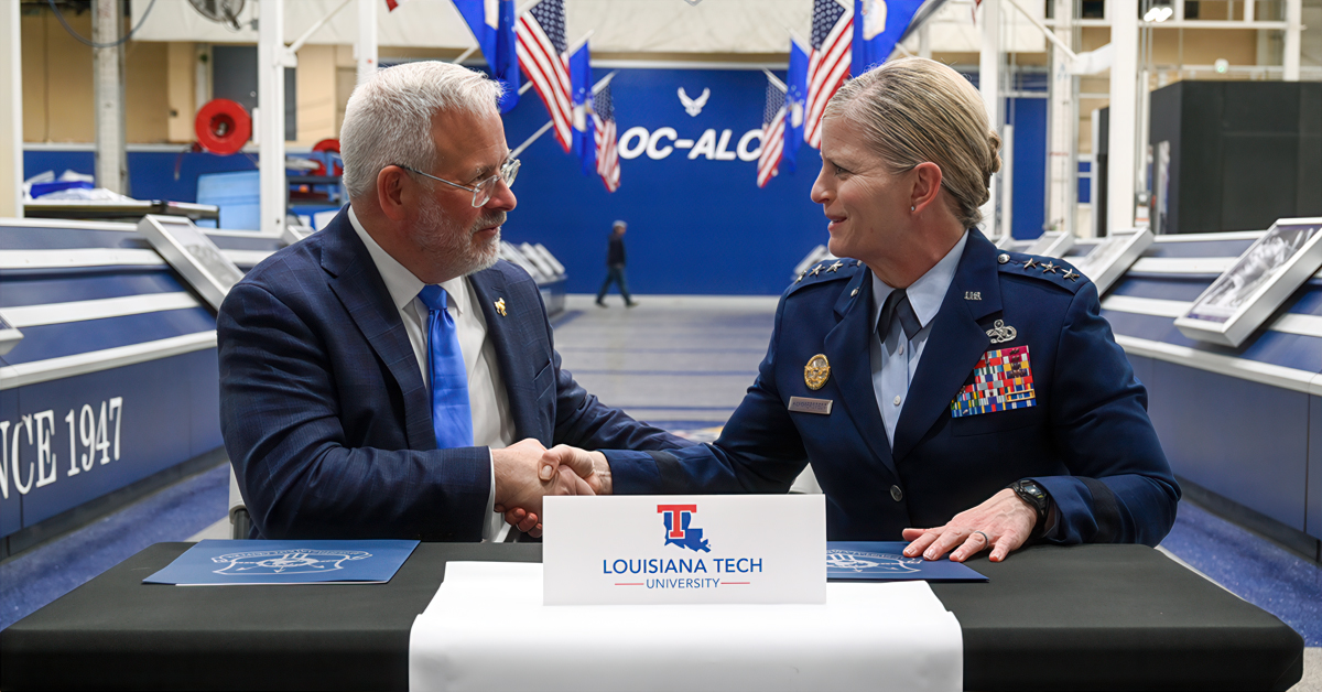Louisiana Tech President Jim Henderson and Air Force Lt. Gen. Jennifer Hammerstedt shake hands at a table after signing documents.