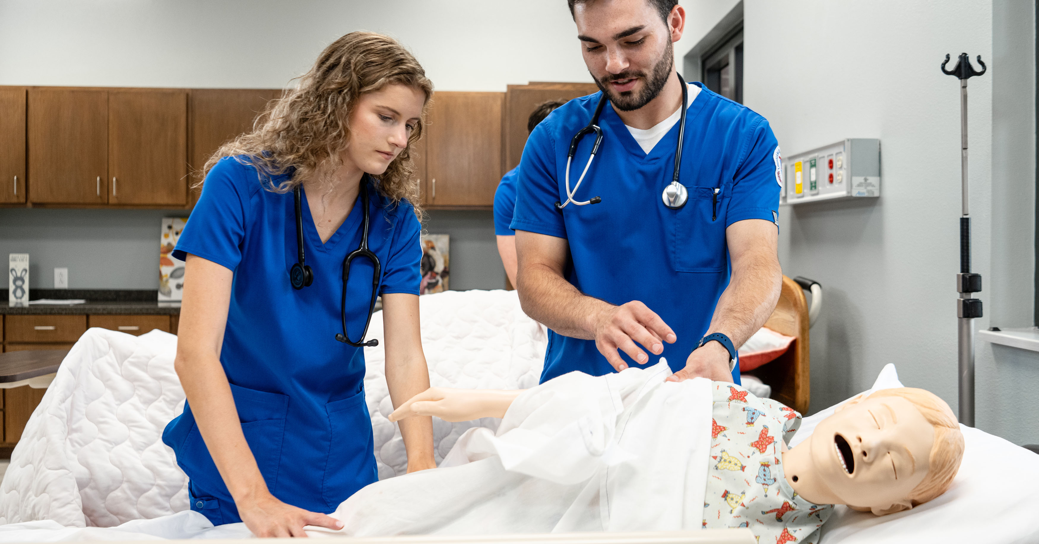 Two nursing students practice on a training dummy in a lab