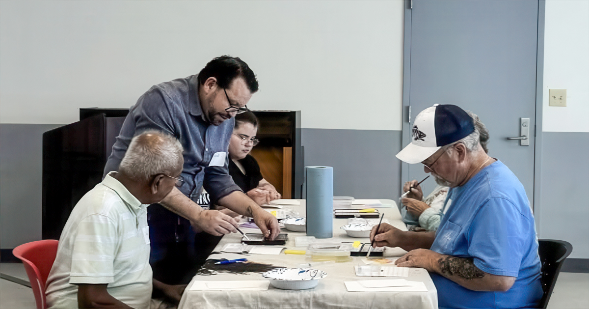 A man guides people through watercolor painting at a table
